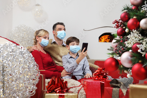 Merry christmas, happy family wear surgical mask, forced to stay at home alone because of the coronavirus, communicates with mobile phone remotely, christmas lockdown concept