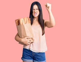 Sticker - Young beautiful caucasian woman holding paper bag with bread annoyed and frustrated shouting with anger, yelling crazy with anger and hand raised