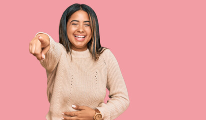 Poster - Young latin girl wearing wool winter sweater laughing at you, pointing finger to the camera with hand over body, shame expression