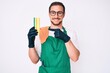 © Krakenimages.com - Young handsome man wearing apron holding scourer smiling happy pointing with hand and finger