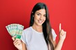 © Krakenimages.com - Young brunette woman holding hong kong 50 dollars banknotes smiling with an idea or question pointing finger with happy face, number one