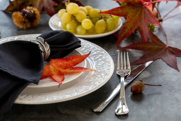 Autumn style dinner table set with red leaves, grapes and a bottle of wine. Selective focus.