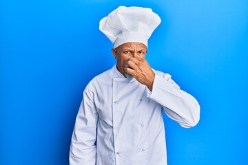 Sticker - Middle age grey-haired man wearing professional cook uniform and hat smelling something stinky and disgusting, intolerable smell, holding breath with fingers on nose. bad smell