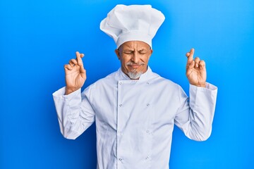 Sticker - Middle age grey-haired man wearing professional cook uniform and hat gesturing finger crossed smiling with hope and eyes closed. luck and superstitious concept.