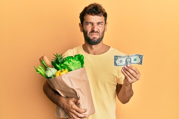 Poster - Handsome man with beard holding groceries and 1 american dollar banknote skeptic and nervous, frowning upset because of problem. negative person.