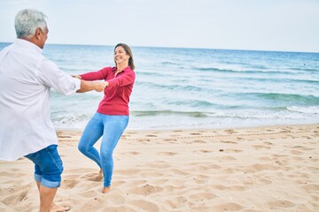 Middle age couple in love dancing at the beach happy and cheerful together