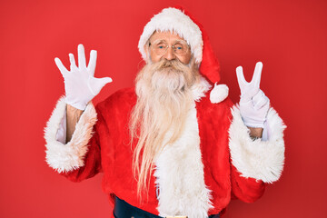 Wall Mural - Old senior man with grey hair and long beard wearing traditional santa claus costume showing and pointing up with fingers number seven while smiling confident and happy.