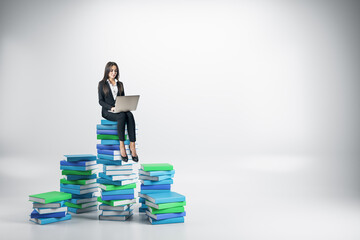 Poster - Young businesswoman with laptop sitting on colored books.