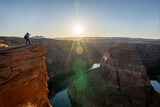 Fototapeta Tęcza - Photographer standing on near edge of cliff with sunflare