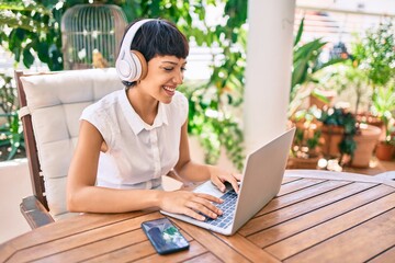 Beautiful woman with short hair sitting at the terrace on a sunny day working from home using laptop