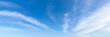 Translucent cirrus cloud stripes float slowly high in a bright blue sky on a sunny day. Panoramic skyscape shot. Weather, meteorology and types of clouds.