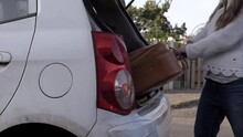 Woman Taking Old Brown Suitcase Out Of Car Boot Wide Shot