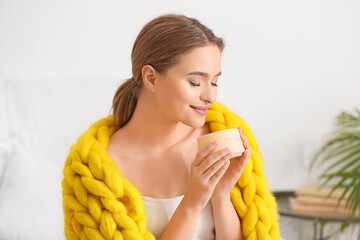 Poster - Happy young woman with warm plaid and cup of coffee at home