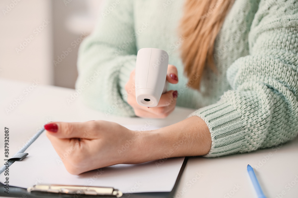Woman with infrared thermometer measuring temperature in office, closeup. Coronavirus epidemic
