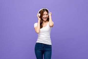 Happy smiling Asian woman wearing headphones listening to music with eyes closed on isolated purple backgroud