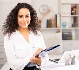 Wall Mural - Elegant businesswoman holding clipboard and welcoming to modern office