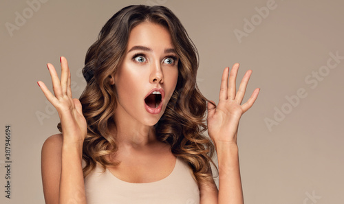 Beautiful shocked and surprised woman screaming and  looking to the side presenting  your product . Curly hair girl amazed . Expressive facial expressions . Beauty and cosmetology