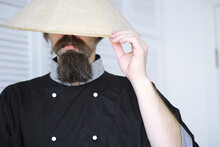 A Hilarious Parody Of An Asian Man In A Vietnamese Hat With A Beard. Portrait. Asian Cafe Chef.
