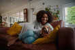© StratfordProductions - Portrait of black woman playing with pet dachshund dog at home sitting on couch