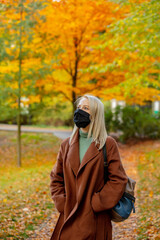 Sticker - Style blonde in face mask and coat on autumn park with maples on background