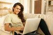 © shurkin_son - Adorable Arabic girl in casual clothes relaxing on couch using laptop, looking at screen with smile, chatting with friends distantly, via group video conference call, enjoying online communication