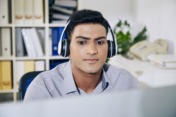Wall Mural - handsome serious young indian software developer listening to music in headphones when programming a