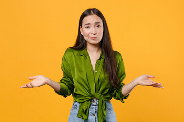 Poster - Confused puzzled upset displeased young brunette asian woman 20s wearing casual basic green shirt standing spreading hands looking camera isolated on bright yellow colour background, studio portrait.