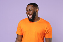 Blinking Cheerful Funny Excited Young African American Man 20s Wearing Basic Casual Orange Blank Empty T-shirt Standing Looking Camera Isolated On Pastel Violet Colour Background, Studio Portrait.