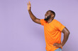 © ViDi Studio - Side view of laughing young african american man in basic casual orange t-shirt standing waving and greeting with hand as notices someone isolated on pastel violet colour background, studio portrait.
