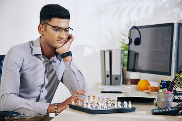Wall Mural - pensive handsome young indian software developer looking at chess board and thinking on next move