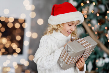 Wall Mural - Happy excited girl child holding Christmas gift box. Child giving a Christmas present in decorated room. Christmas and people concept. New Year Happy holidays. kid satisfied with present.