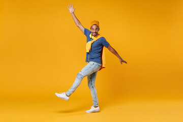 Wall Mural - Full length side view of smiling cheerful young african american man 20s wearing blue t-shirt hat standing rising spreading hands and legs isolated on bright yellow colour background, studio portrait.