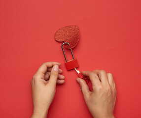 two female hands hold a metal lock and keys on a red background