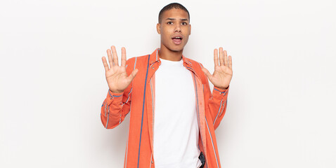 Wall Mural - young black man feeling stupefied and scared, fearing something frightening, with hands open up front saying stay away