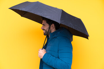 Wall Mural - Man holding an umbrella over isolated yellow background with happy expression