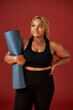 © Roman - portrait of beautiful chubby african woman going to do sport exercises alone, hold blue mat in hands, posing at camera, wearing black top and leggins