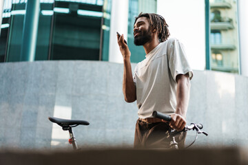 Wall Mural - African american guy talking on cellphone while standing with bicycle