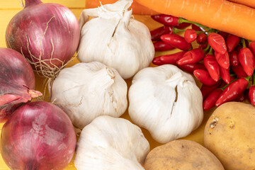 Wall Mural - Red onions garlic potatoes carrots and red chili on a yellow wood background