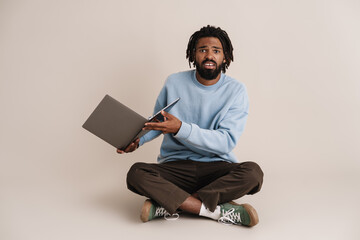 Unhappy african american guy sitting with laptop on floor