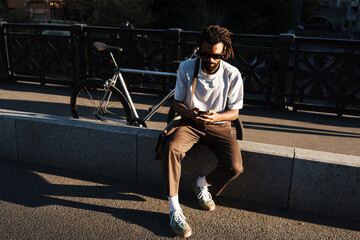 Wall Mural - African american guy using cellphone while sitting at city street