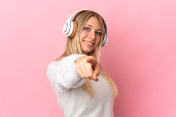 Poster - Young blonde woman isolated on pink background listening music and pointing to the front