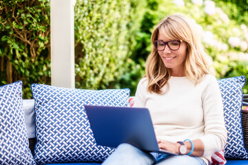 Happy mature woman having video call while sitting in the garden at home