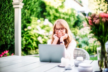 Happy mature woman having video call while sitting in the garden at home