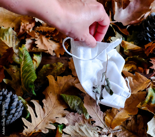 Surgical white mask thrown over dried leaves on the ground during the autumn epidemic, face mask, medical mask, fall season, nature, pandemic, Person taking the medical mask off the ground