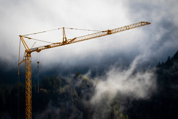 orange construction site crane with foggy misty forest in background with fading white to top