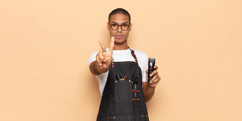 Wall Mural - young black man smiling and looking happy, carefree and positive, gesturing victory or peace with one hand