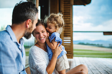 Wall Mural - family with small daughter sitting on patio of wooden cabin, holiday in nature concept.