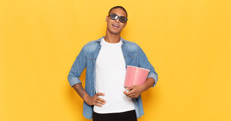 Sticker - young black man smiling happily with a hand on hip and confident, positive, proud and friendly attitude