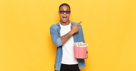 Wall Mural - young black man looking excited and surprised pointing to the side and upwards to copy space