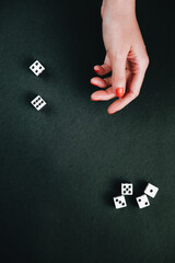 Female hand tossing dices. White square dices against a black background.